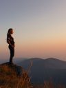 Hipster young girl with backpack enjoying sunset on peak of fogg