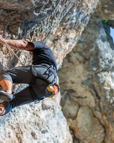 Man climbing on rock against blue sky background