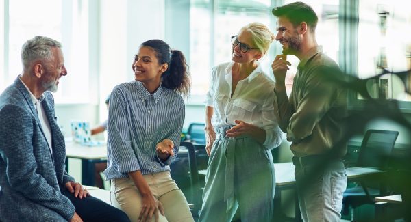 Group of cheerful business people communicating, discussing something and smiling while standing in the modern office or coworking space