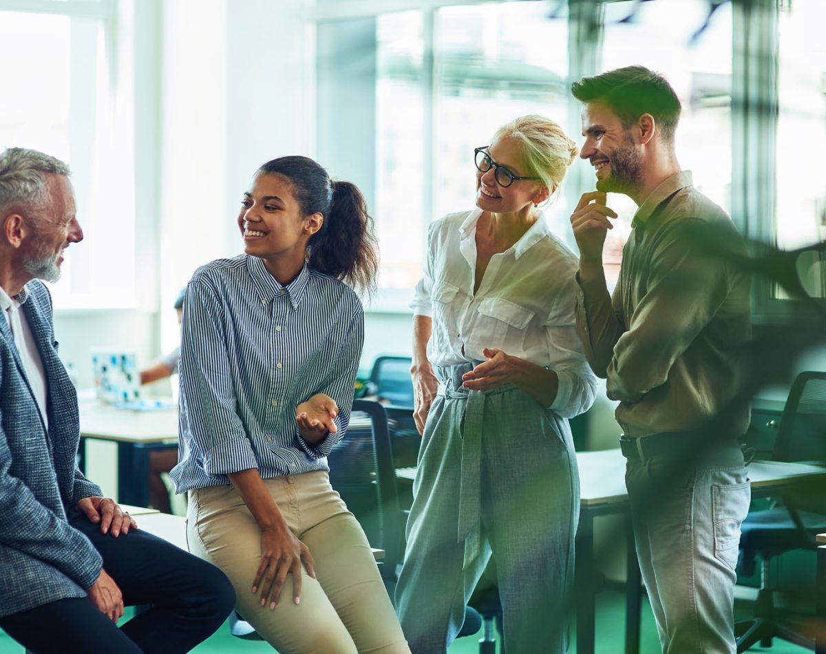 Group of cheerful business people communicating, discussing something and smiling while standing in the modern office or coworking space